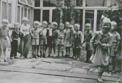 876949 Afbeelding van een grote groep kleuters die toekijkt bij het touwtjespringen op de binnenplaats van het Klooster ...